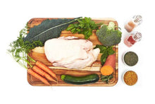 Load image into Gallery viewer, Raw turkey breast on a wooden cutting board with organic vegetables and herbs arranged around it.