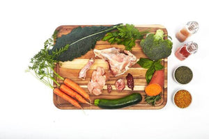 Fresh ingredients for Smallbatch Lightly Cooked Chicken: chicken, carrots, zucchini, broccoli, herbs, and spices on a wooden chopping board.